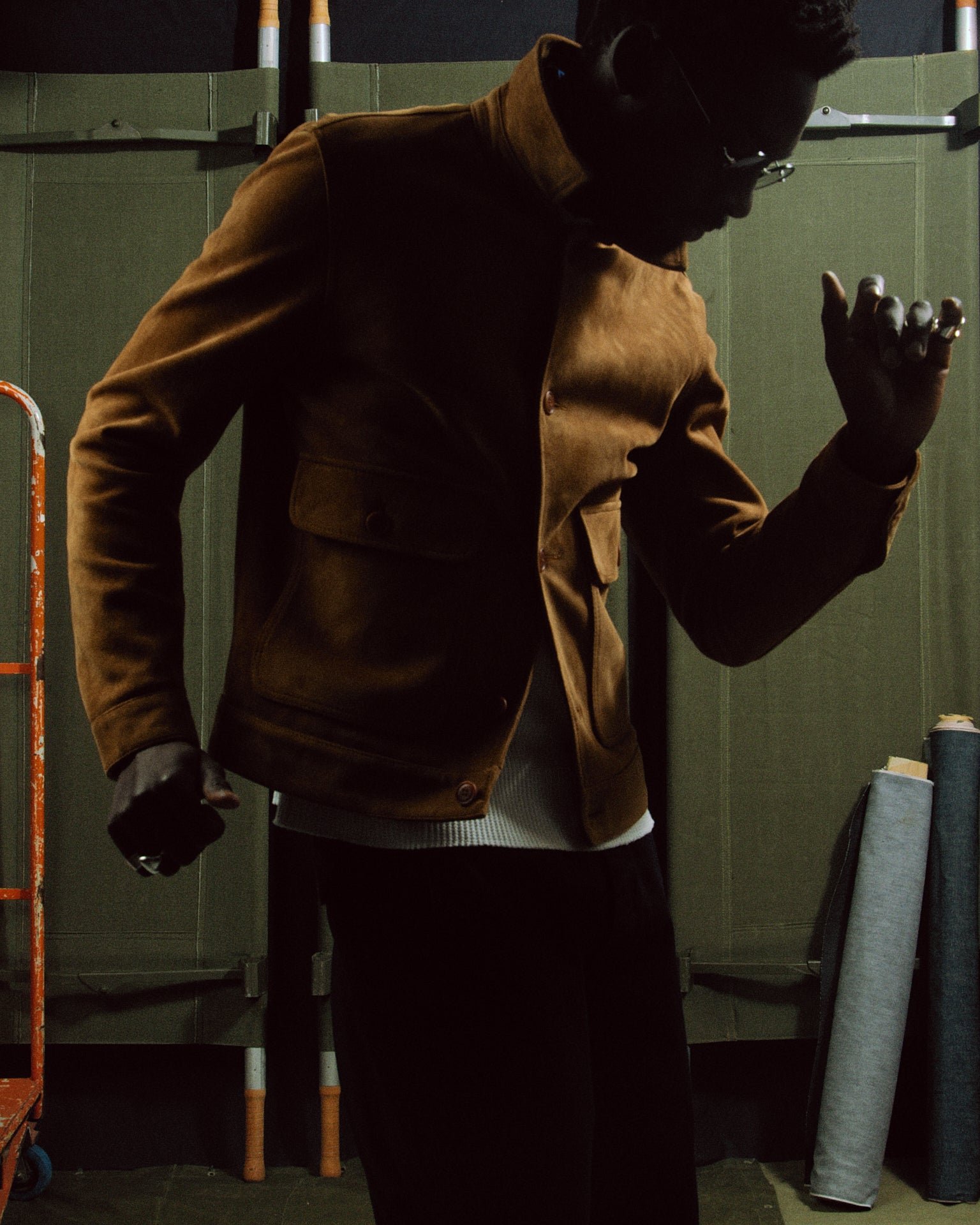 Blouson en daim et nubuck pour homme, couleur cognac, porté par un mannequin dans le style d'un blouson similaire à celui porté par Brad Pitt. Le mannequin danse le swing rock'n roll dans l'atelier de champ de manœuvres, avec des tissus selvedge en arrière-plan.
