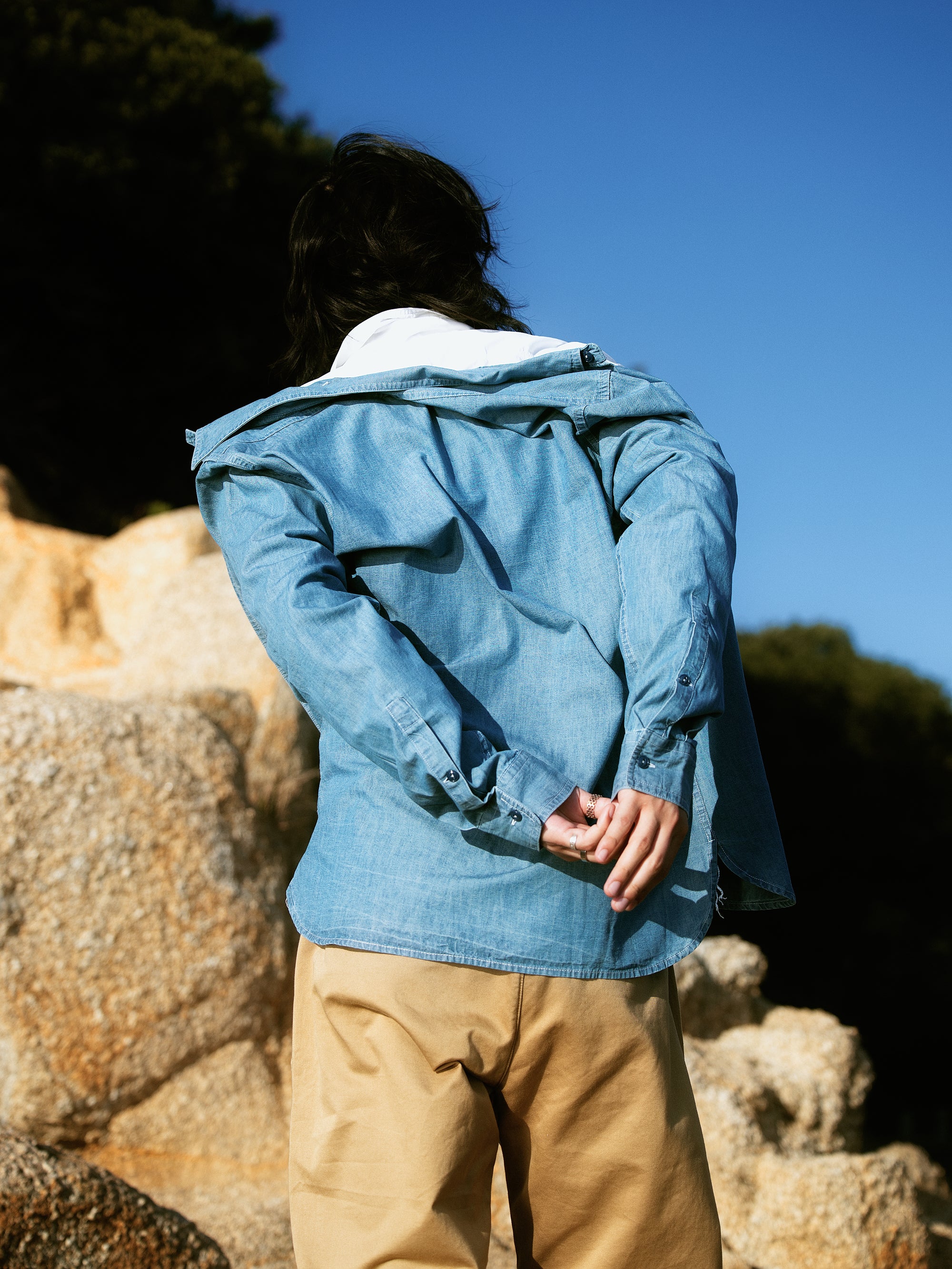 Vue de dos d'une chemise en denim bleu clair Champ de Manoeuvres portée sur t-shirt blanc avec pantalon beige, détails de la coupe et finitions visibles