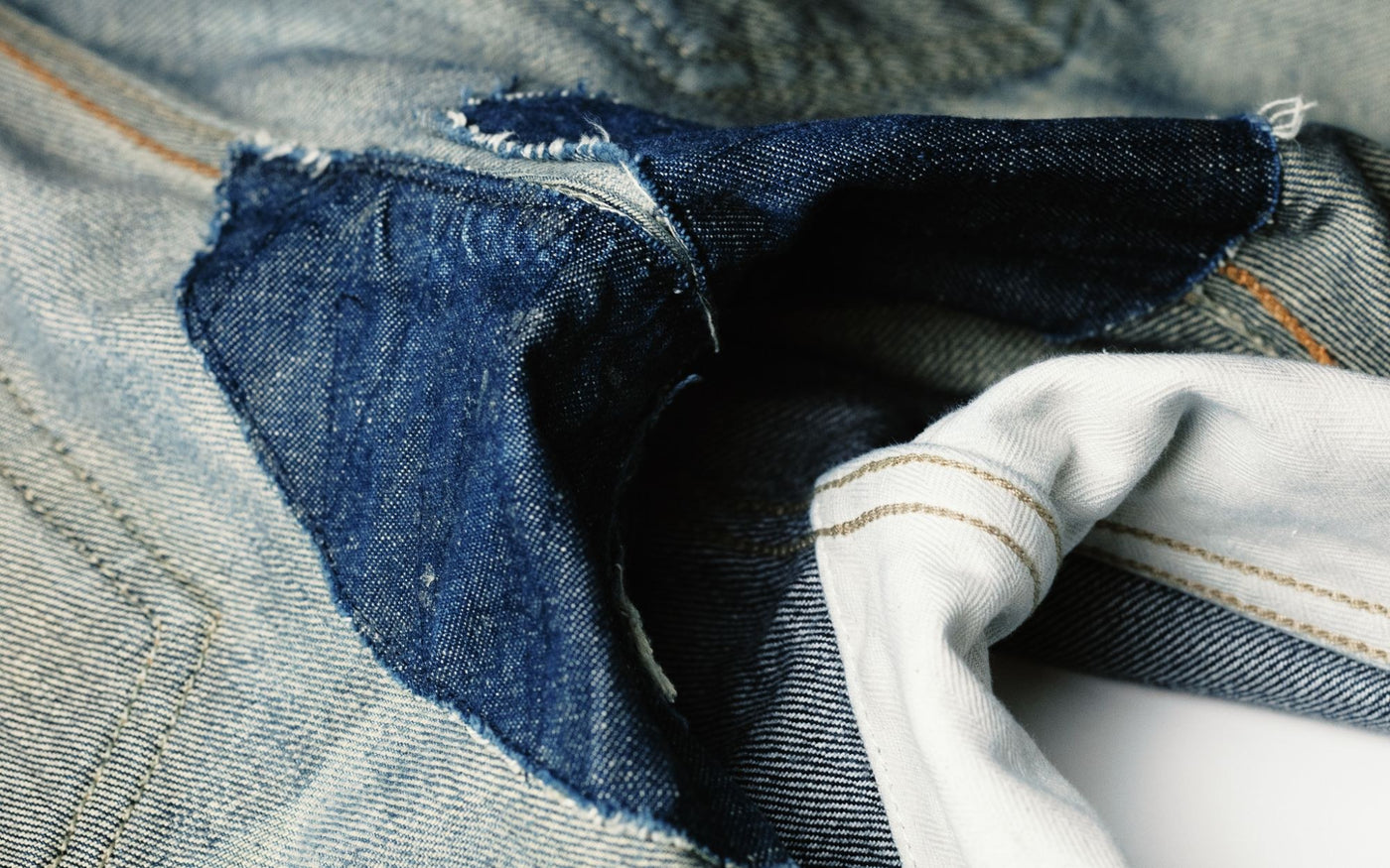 Entrejambe de jean réparé dans un autre atelier par une pièce de denim cousue par-dessus