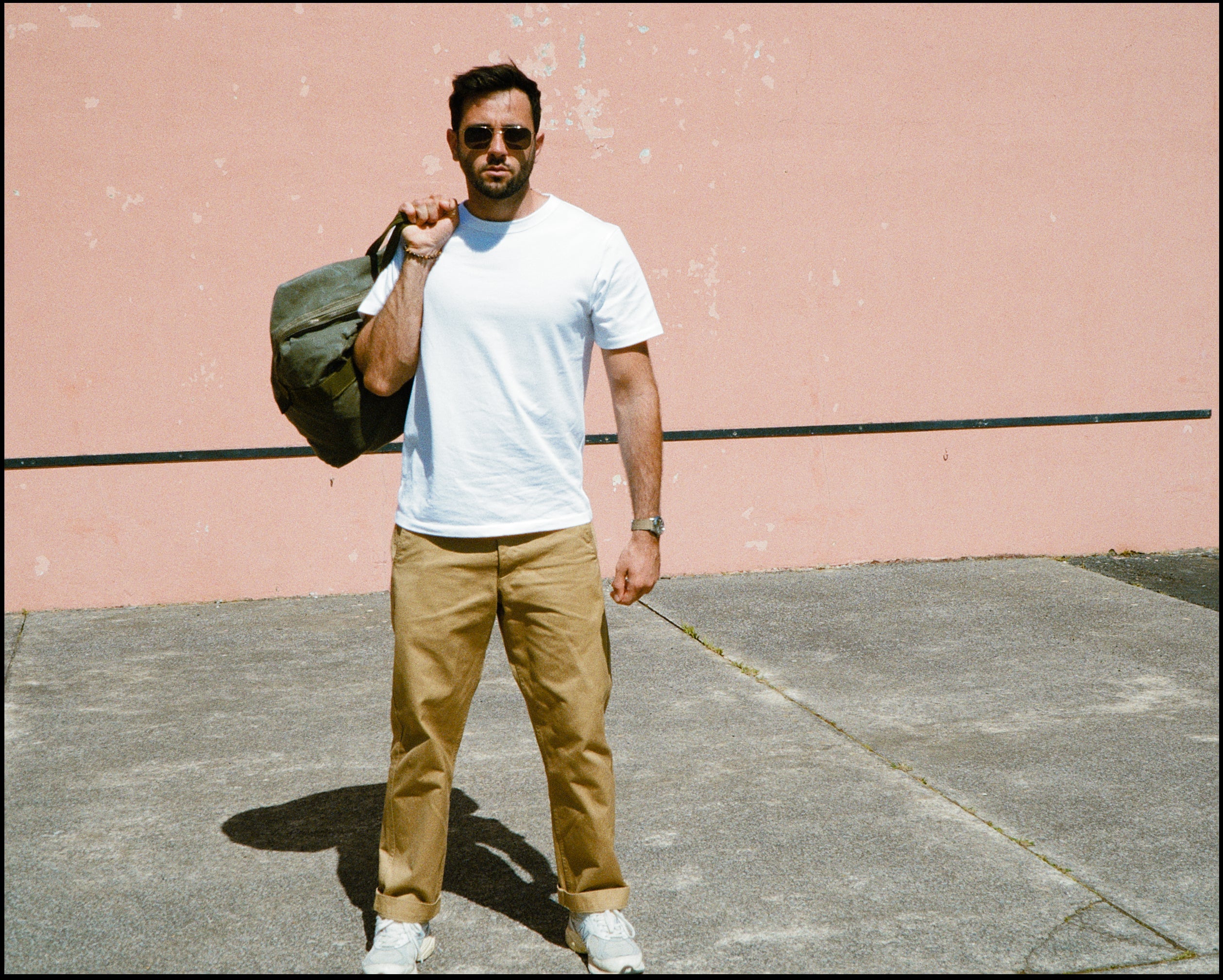 t-shirt colletage homme blanc porté avec un chino en gabardine sable et un sac militaire dans le sud de la france pour champ de manoeuvres