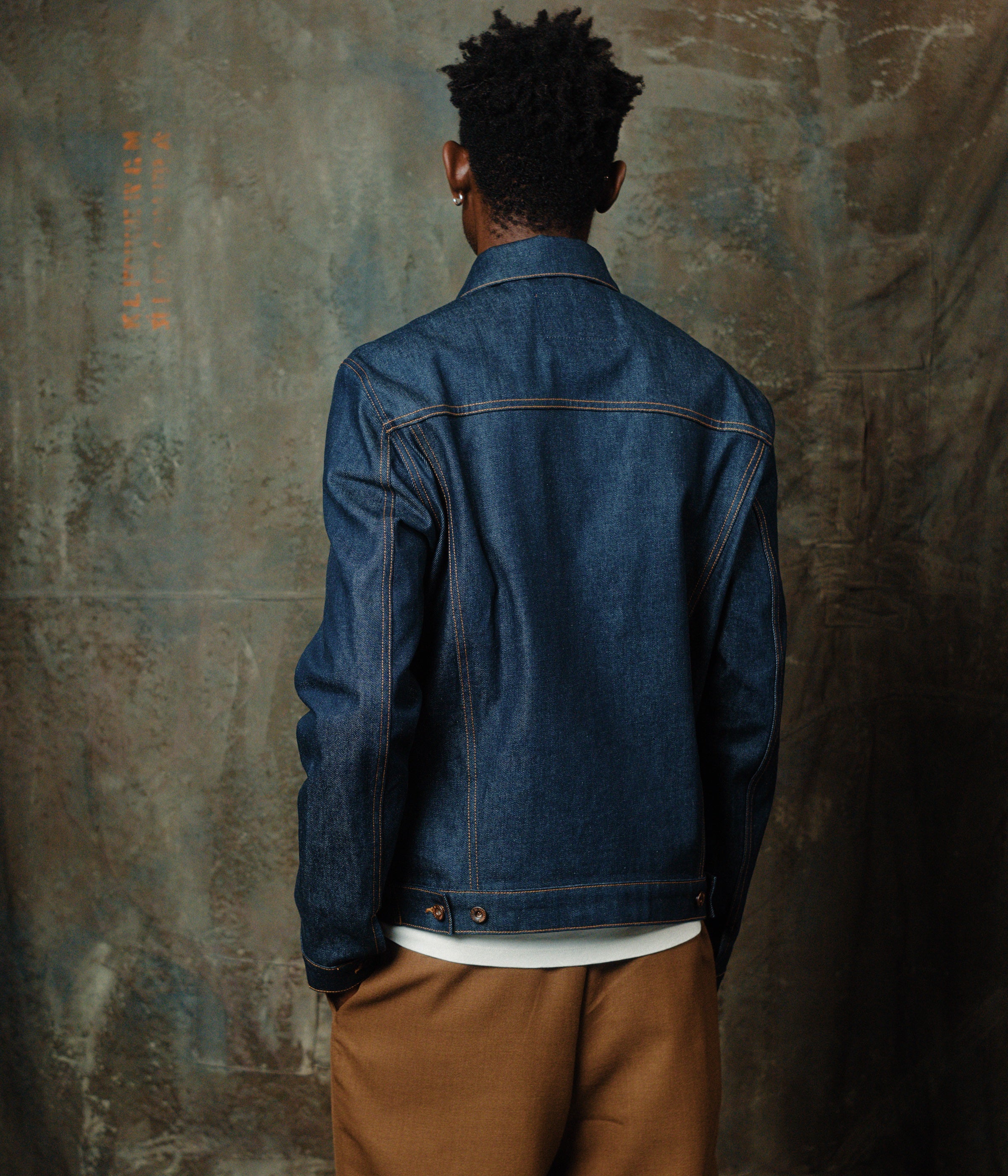 vue de dos de notre blouson en jean brut avec un mannequin dans un atelier de couture et décor artistique