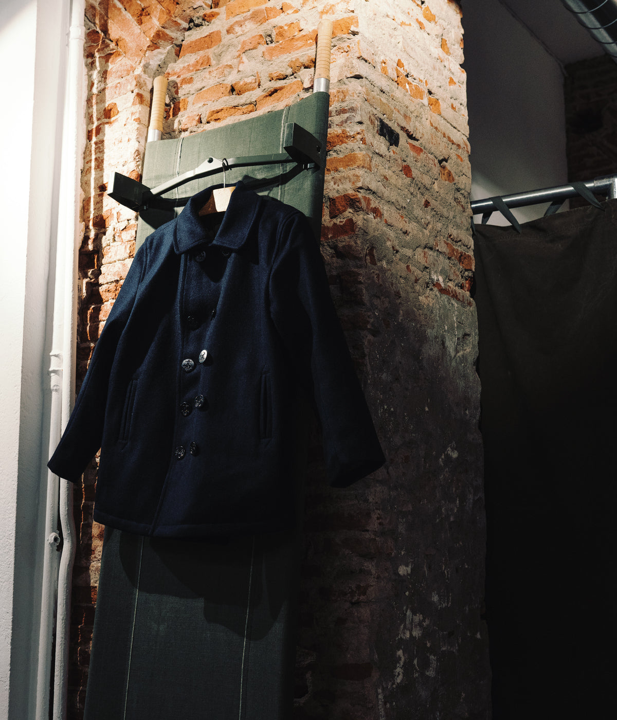 Caban de laine marine suspendu à un panneau de toile, boutique Champ de Manœuvres à Toulouse