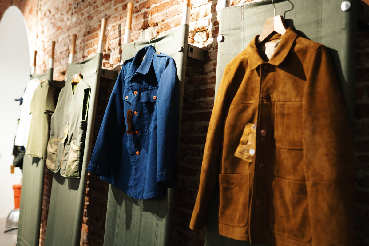 Vestes de travail et chemises suspendues au mur de brique de la boutique Champ de Manœuvres a Toulouse