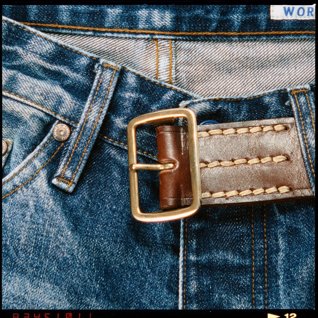 Ceinture en cuir à simple ardillon portée sur un jean délavé, boucle en laiton et couture sellier écrue en gros plan