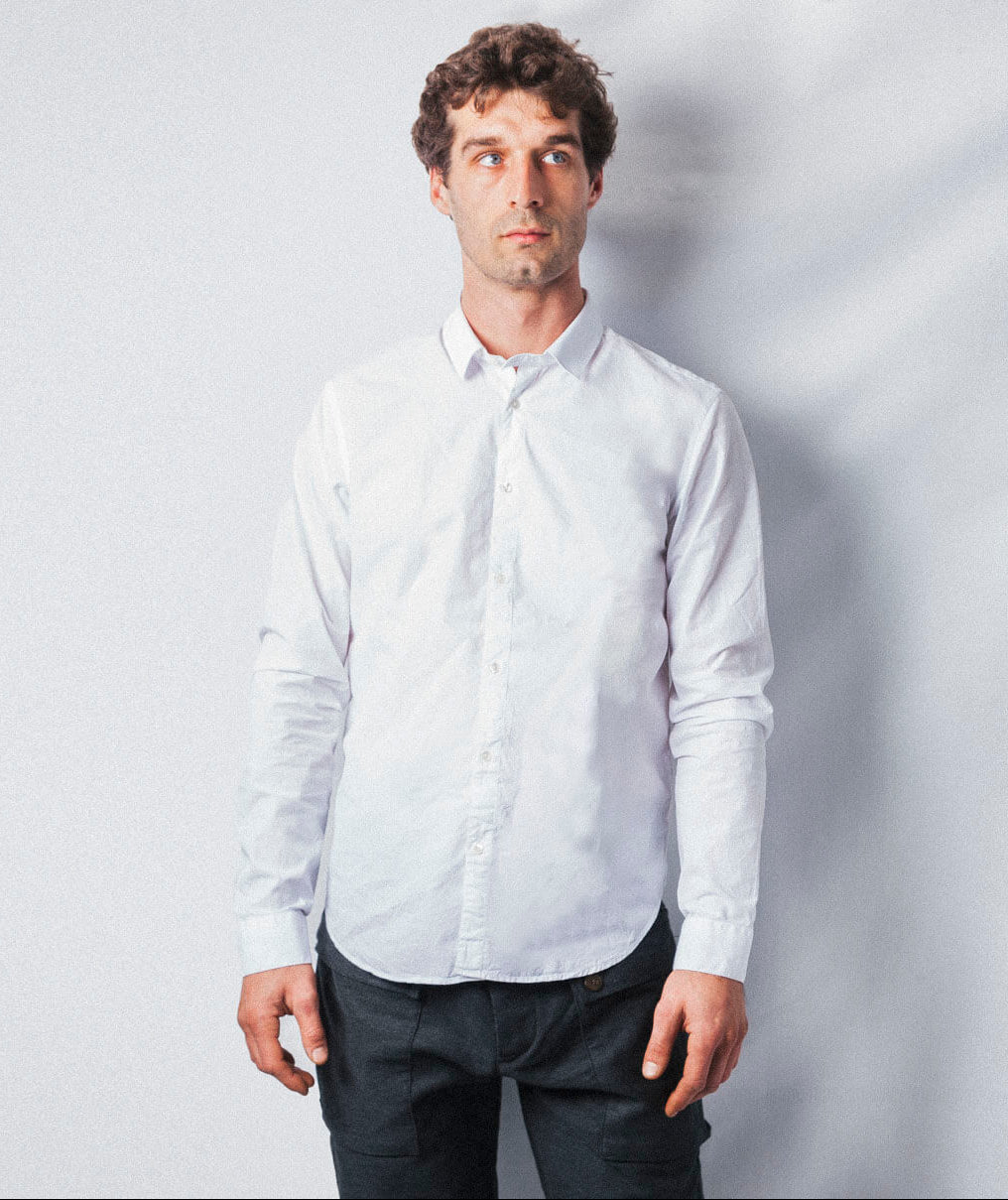 Cette vue de devant présente Ben portant une chemise blanche en taille M. La pièce affiche une coupe slim ajustée au corps et est conçue dans une matière au toucher papier ultra douce. Sa silhouette épurée met en avant un col classique et une boutonnière centrale.