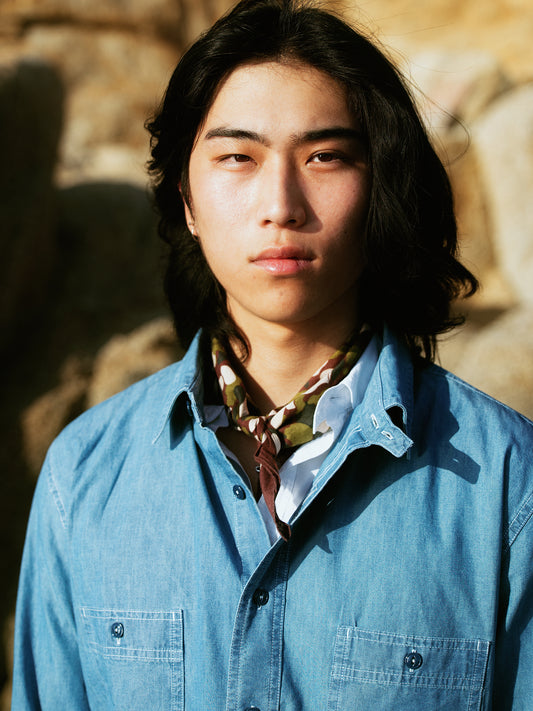 Chemise de travail en denim bleu clair Champ de Manoeuvres portée avec foulard motif camouflage, vêtement authentique inspiré du workwear"