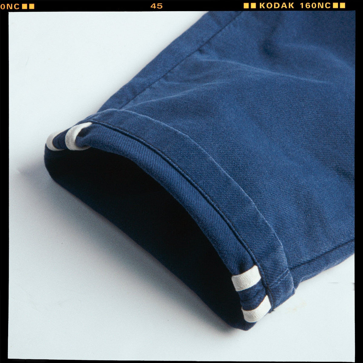 Détail du bas de jambe roulé du Chino Slack Hydron bleu, ourlet et coutures apparentes, cadre de pellicule Kodak