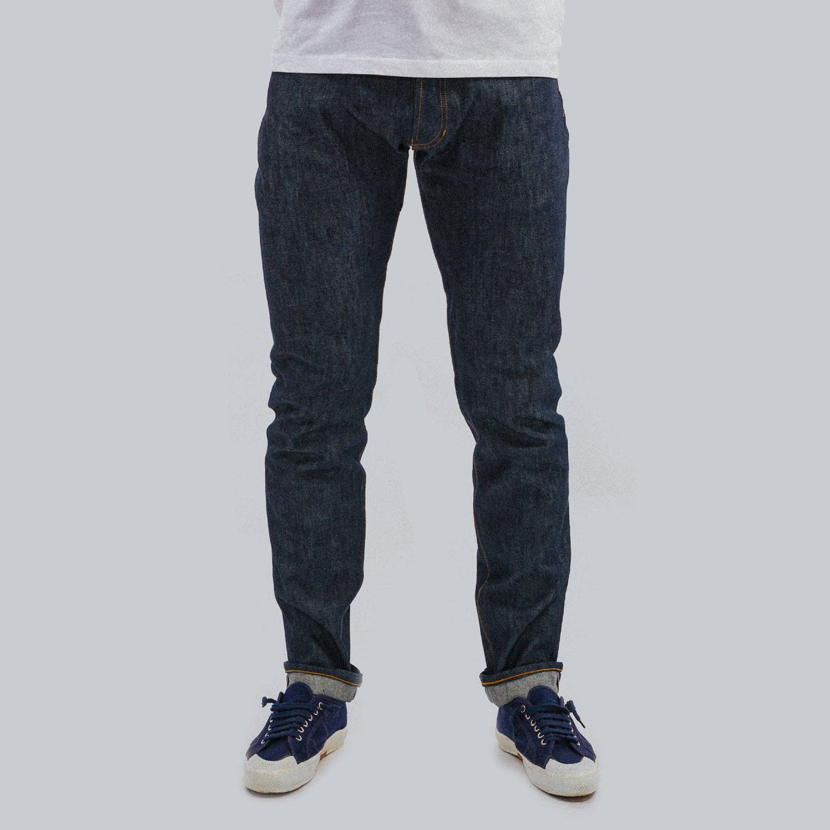 Jeans selvedge 13 oz brut porté à revers roulés avec des sneakers marine, vue de face en pied — Champ de Manoeuvres