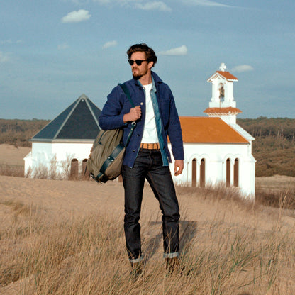 Mannequin portant une veste de travail et un jean selvedge dans le désert devant une église ou un pensionnat abandonné.